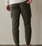 Back view of the Comfort Terry Jogger pants from The Normal Brand. Shown in color dusty olive green. The Jogger has draw strings at the waist, side pockets for your hands, and pockets on both legs, and a rear back pocket on the right side.